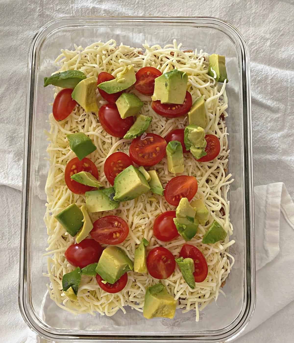 Diced tomatoes and diced avocado on top of layered bean dip