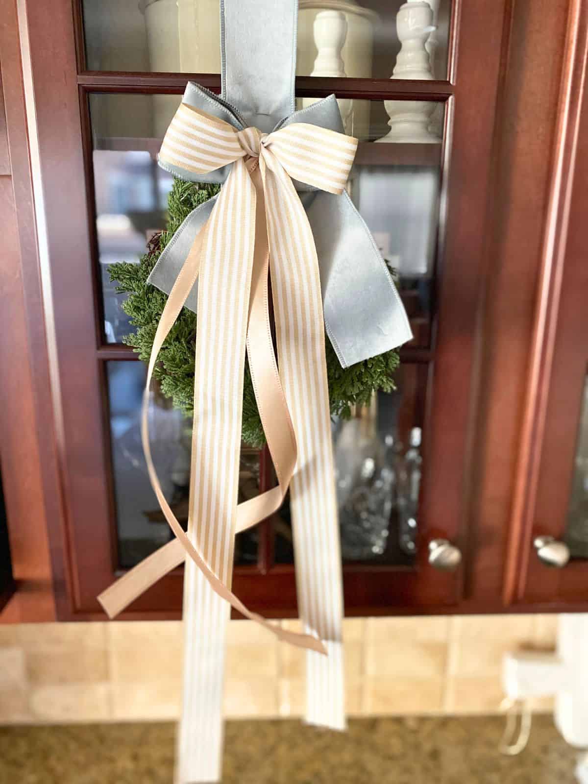 wreath decorated with taupe and blue ribbon hanging on glass cabinet door