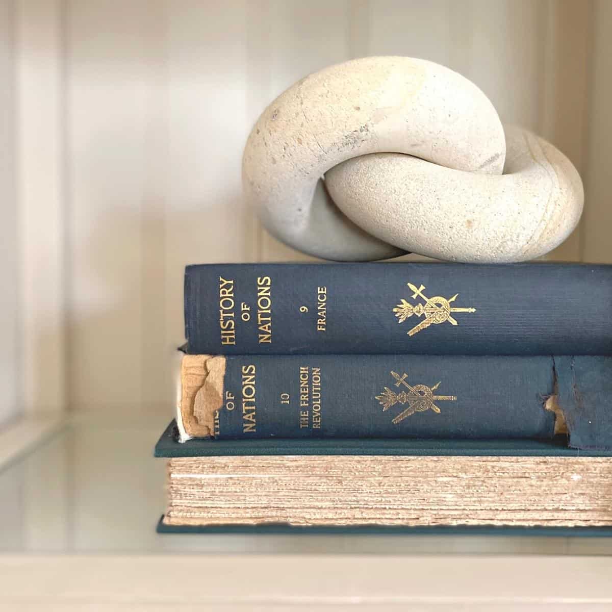 Three navy with gold filigree antique books and white twist object.