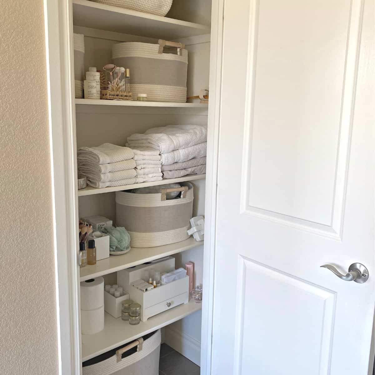 Bathroom closet organized with baskets, folded linens and hair tools