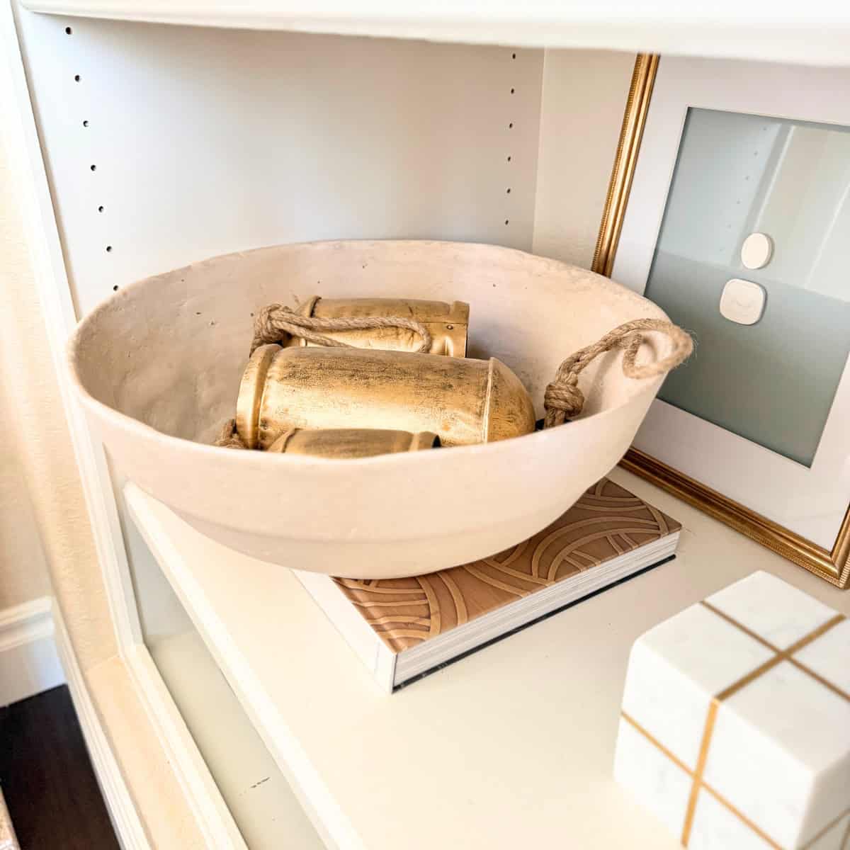 large brass bells in a paper mache bowl on a shelf