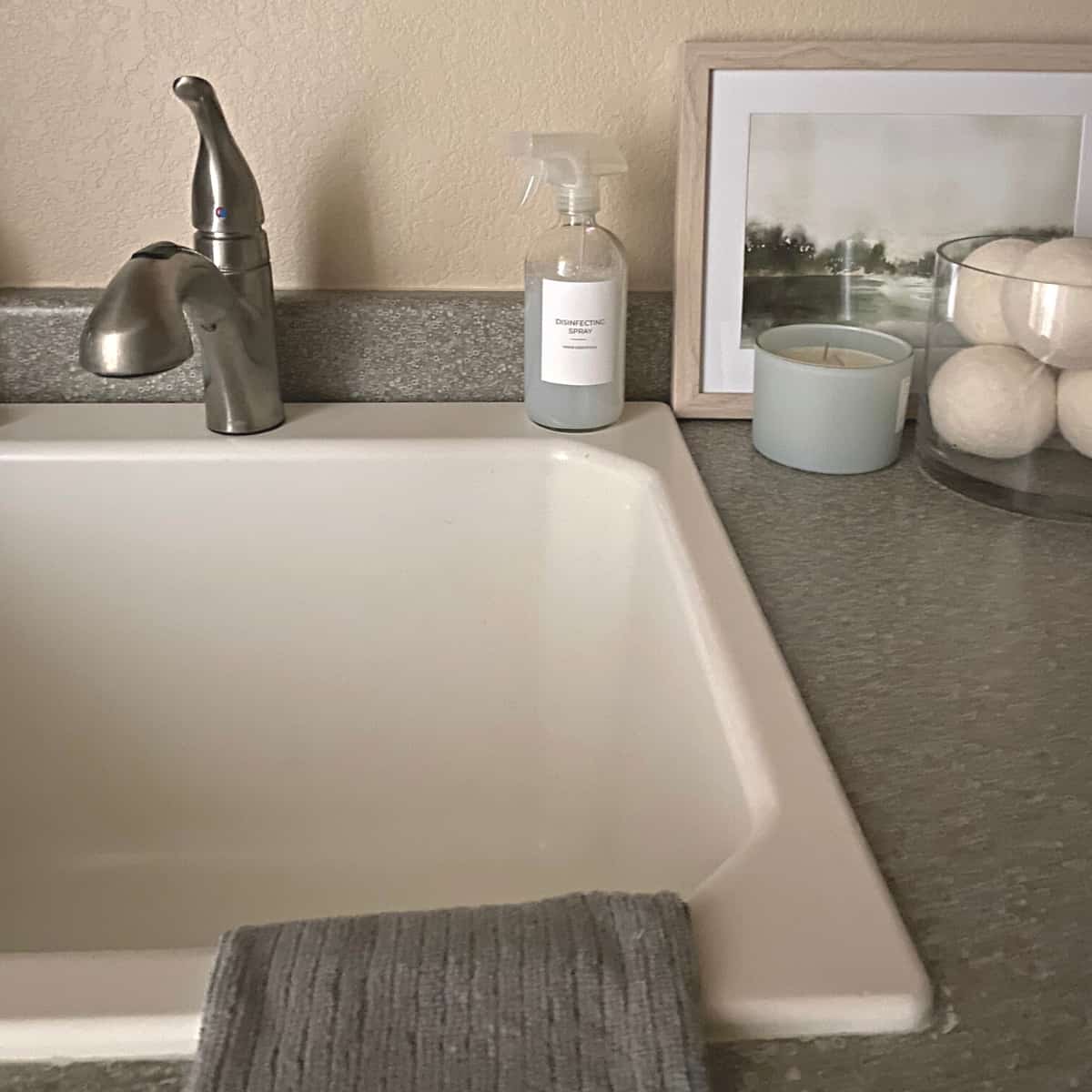 Disinfecting spray in glass spray bottle sits on laundry sink