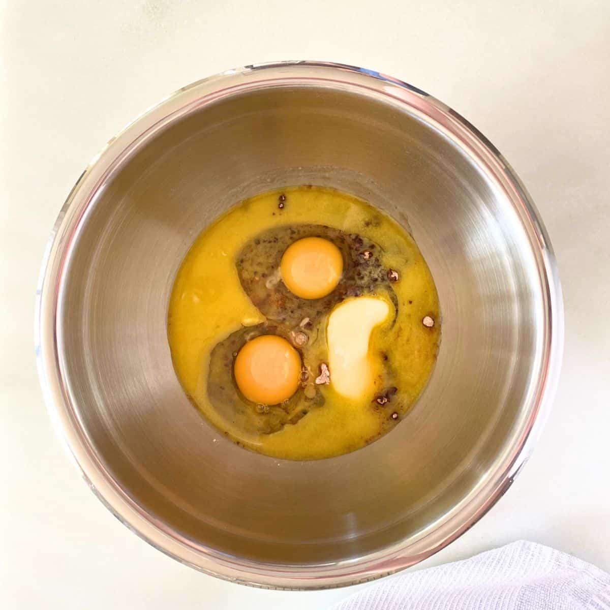 Wet brownie ingredients on top of dry ingredients in a stainless steel mixing bowl