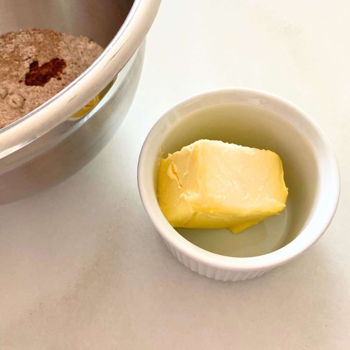 White ramekin of softened butter next to a stainless steel mixing bowl