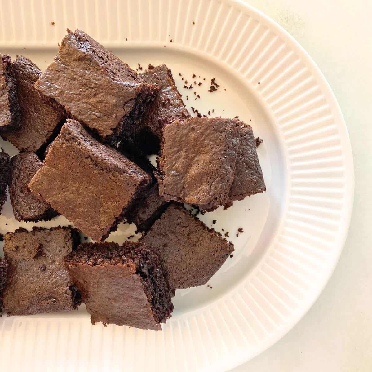 Baked brownies cut into squares stacked on a fluted white porcelain serving platter