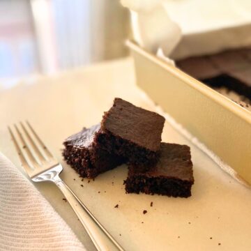 Baked brownies cut into squares stacked on a white marble pastry board next to a silver fork