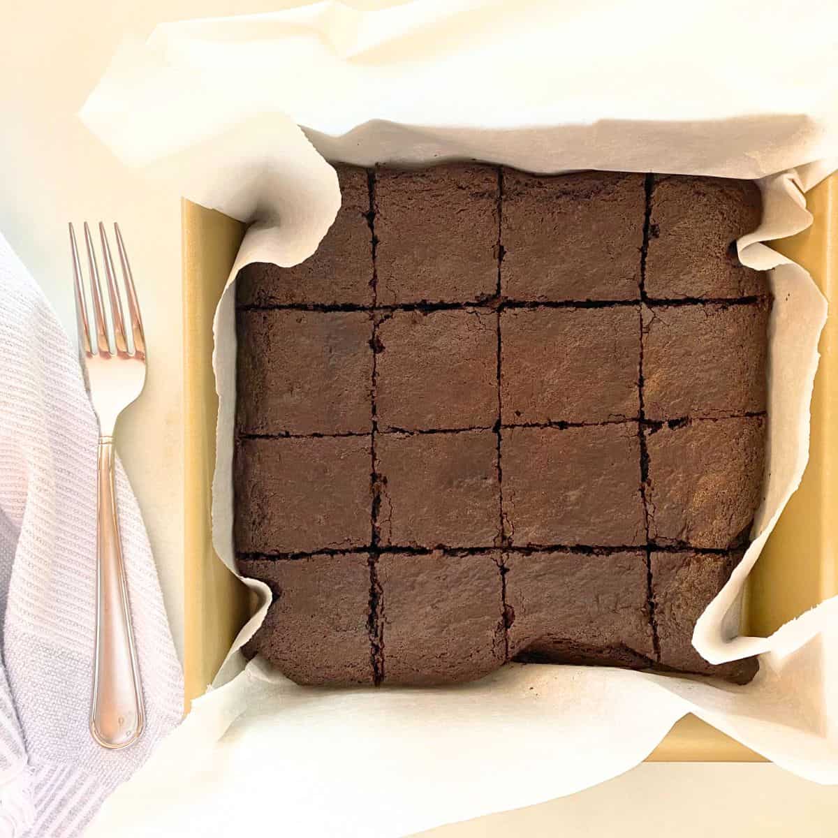 Baked brownies cut into 16 squares in a gold baking pan lined with parchment paper