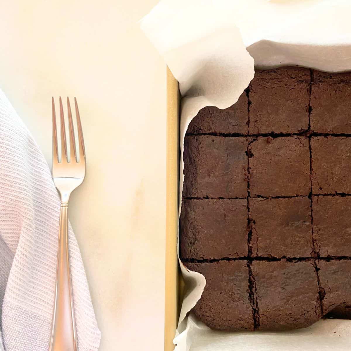 Baked brownies cut into squares in a gold baking pan lined with parchment paper