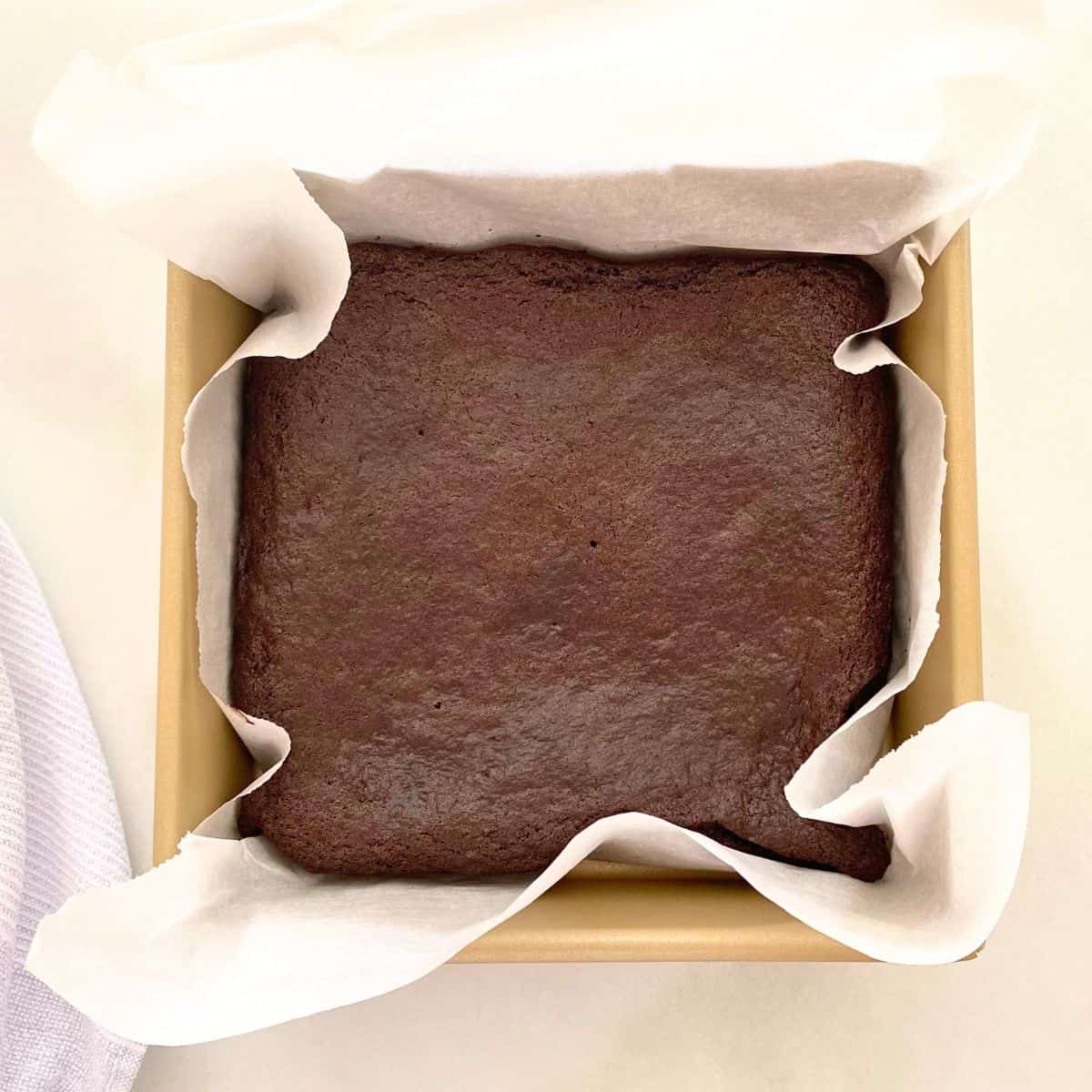 Baked brownies in a gold baking pan lined with parchment paper