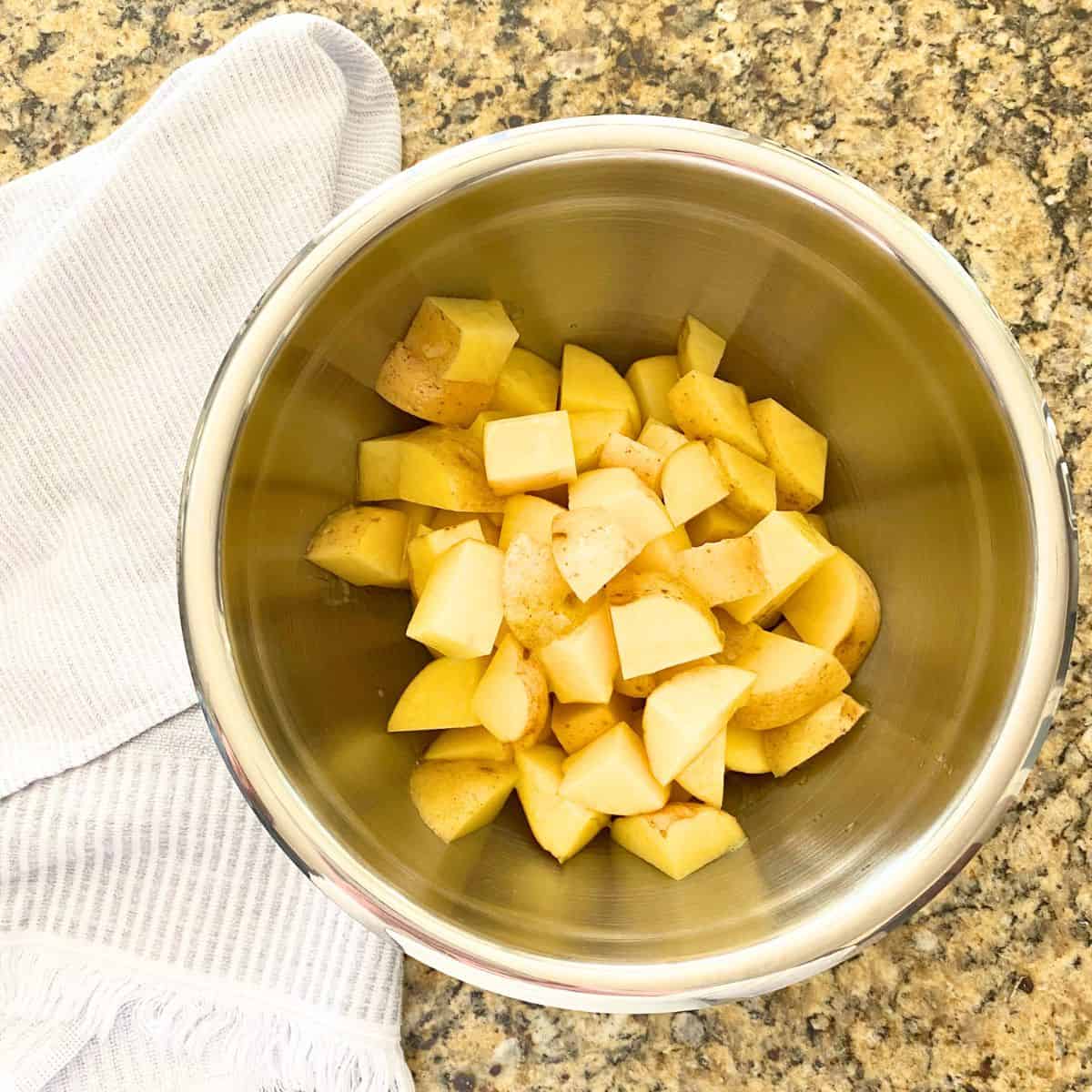 Raw buttered yellow potatoes in a stainless steel mixing bowl
