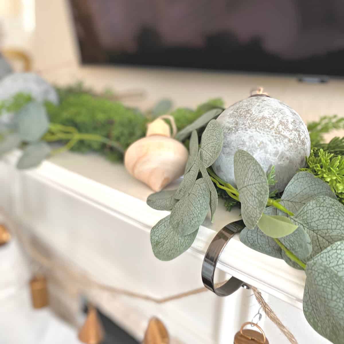 Top of a fireplace mantel decorated for Christmas with greenery garland and neutral ornaments