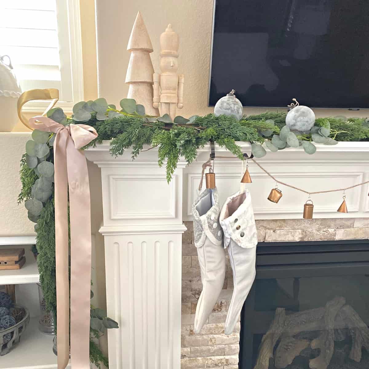 Fireplace mantel decorated for Christmas with greenery garland, blush pink ribbon bow, stockings and ornaments