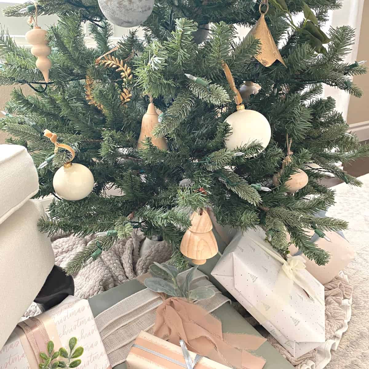 Neutral Christmas ornaments adorn a Christmas tree with presents beneath