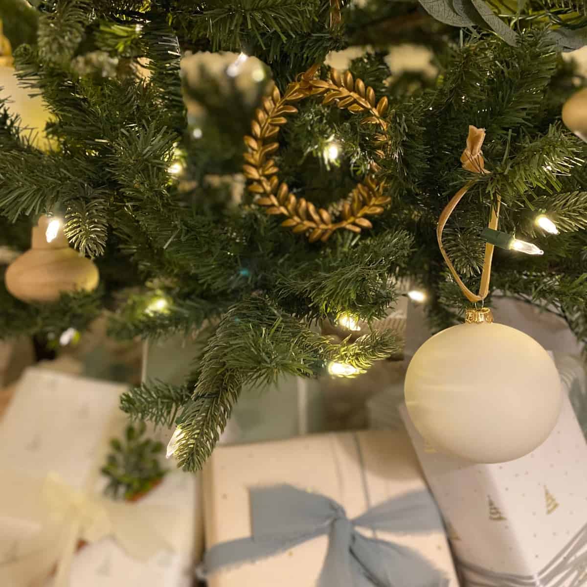 Matte white glass ball ornament and a brass laurel wreath Christmas ornament hangs above neutral presents