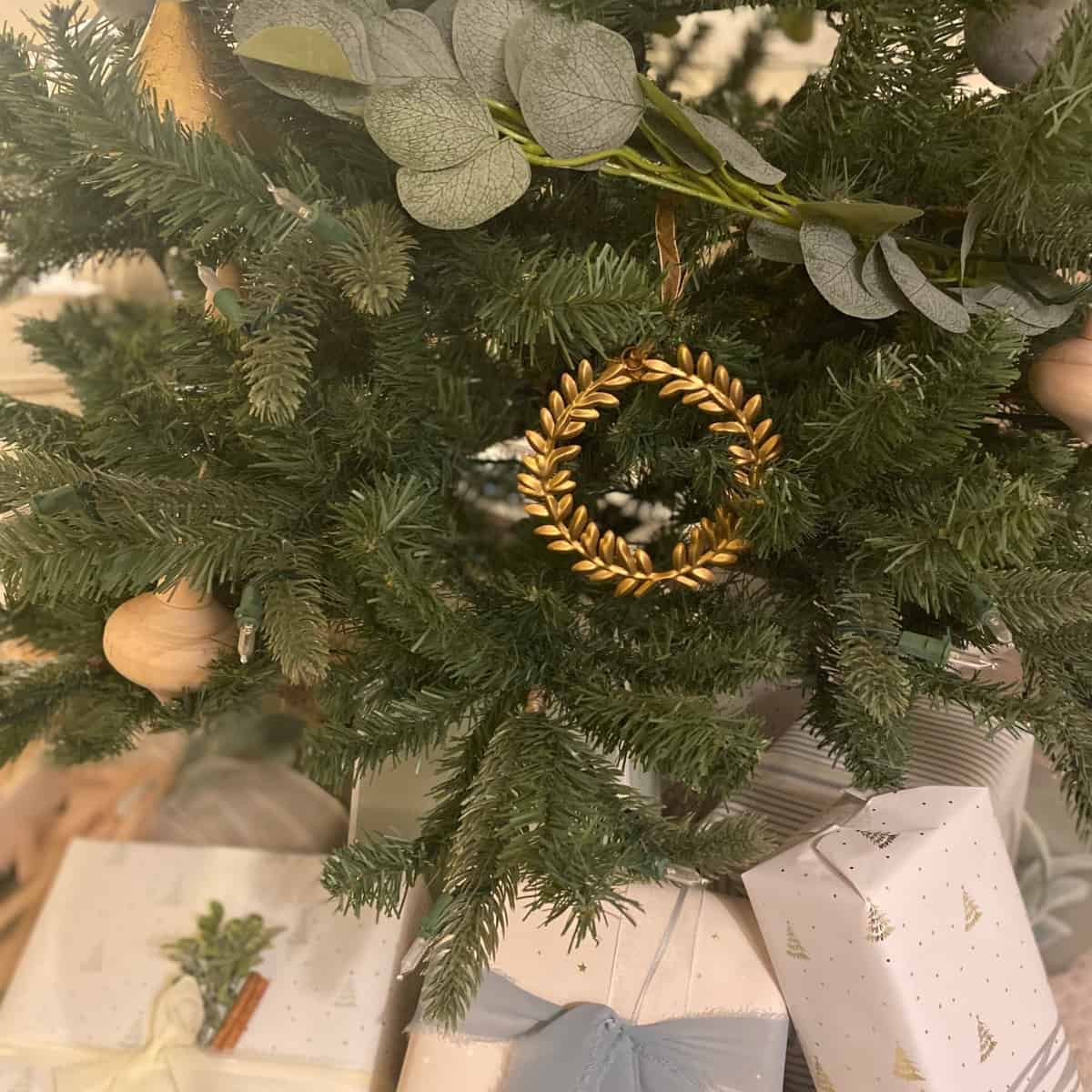 Brass laurel wreath Christmas ornament hangs above neutral presents