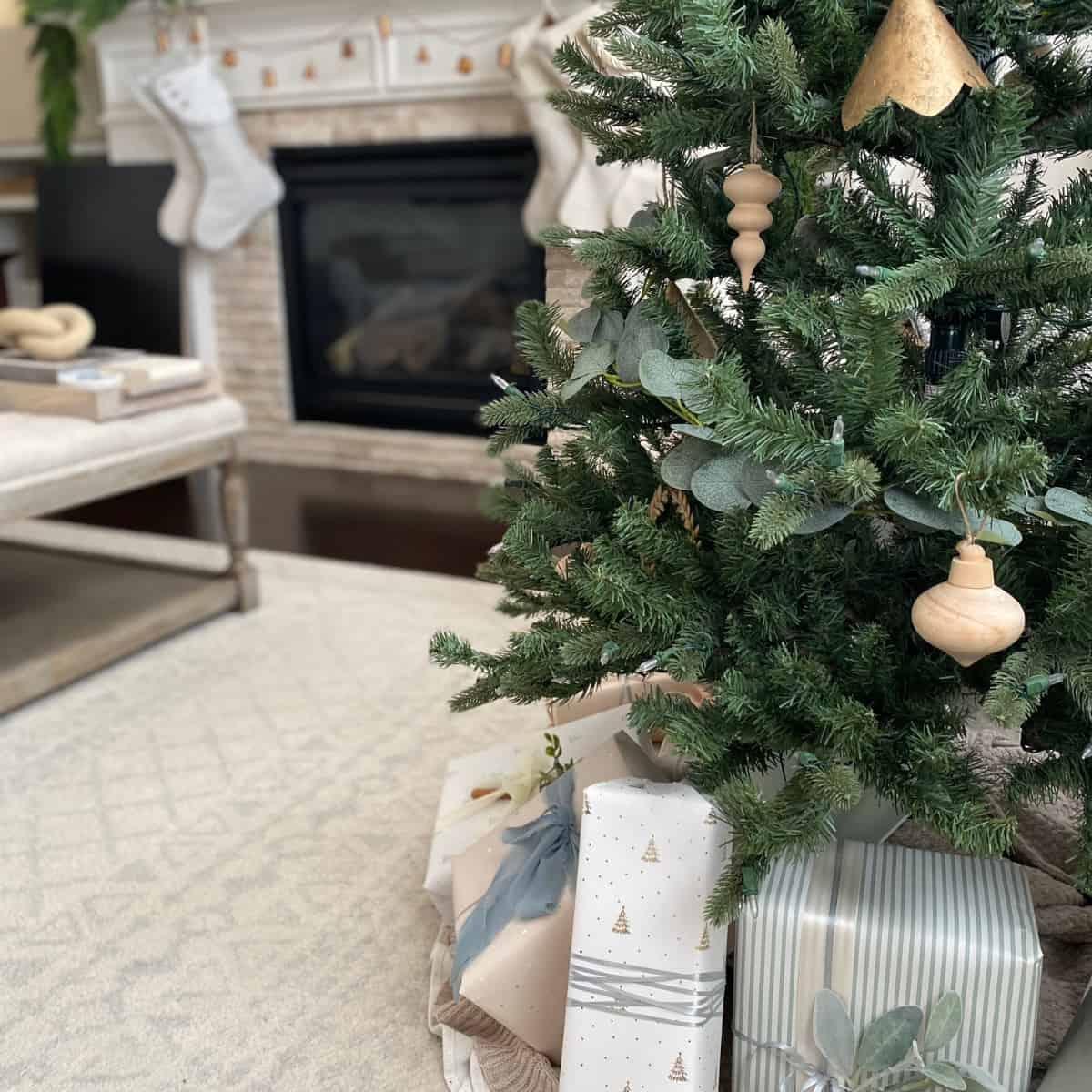 Mid-Christmas tree decorated in neutral ornaments with gifts wrapped in neutral wrapping paper below