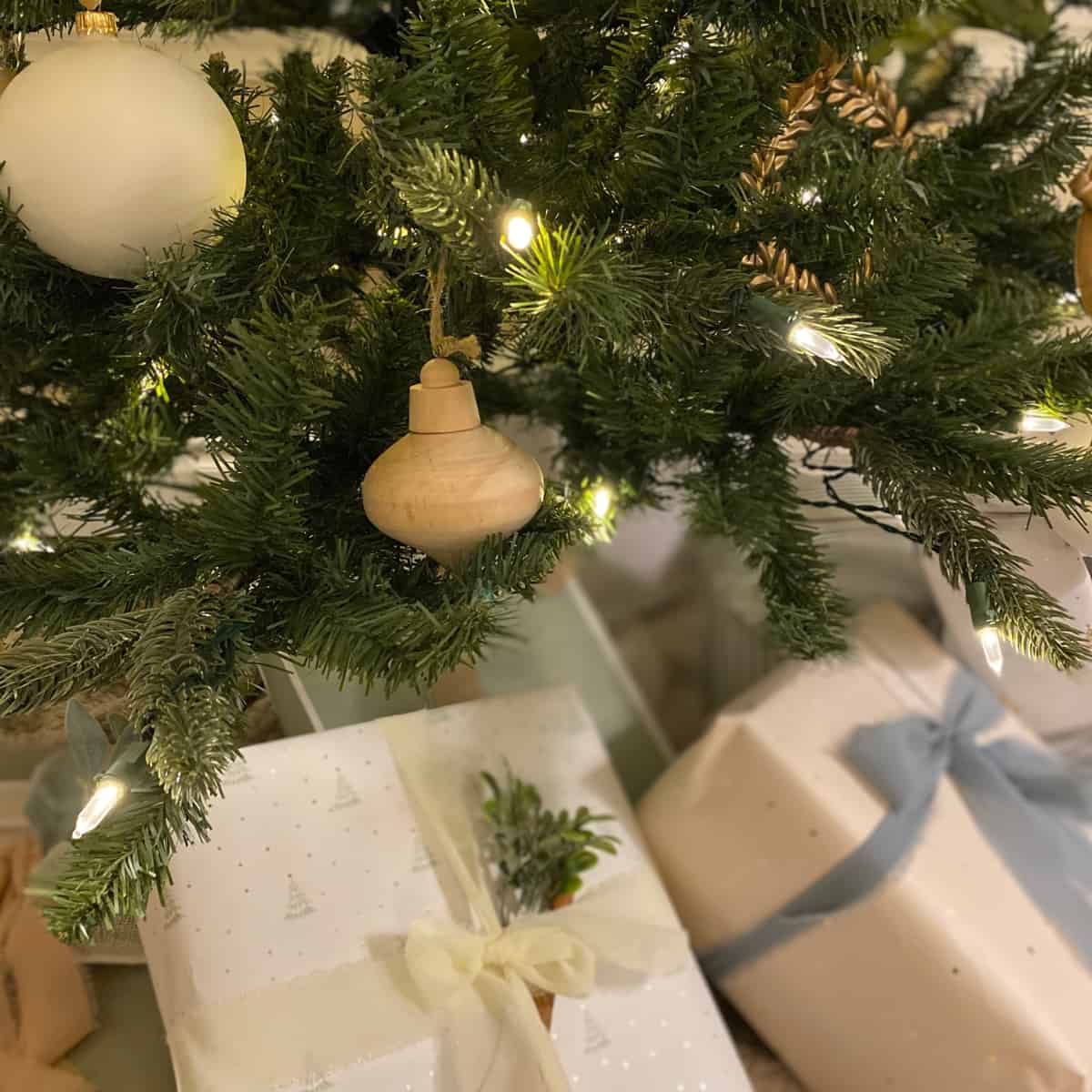 Wood and white tree Christmas ornaments on a tree, with neutral wrapped presents