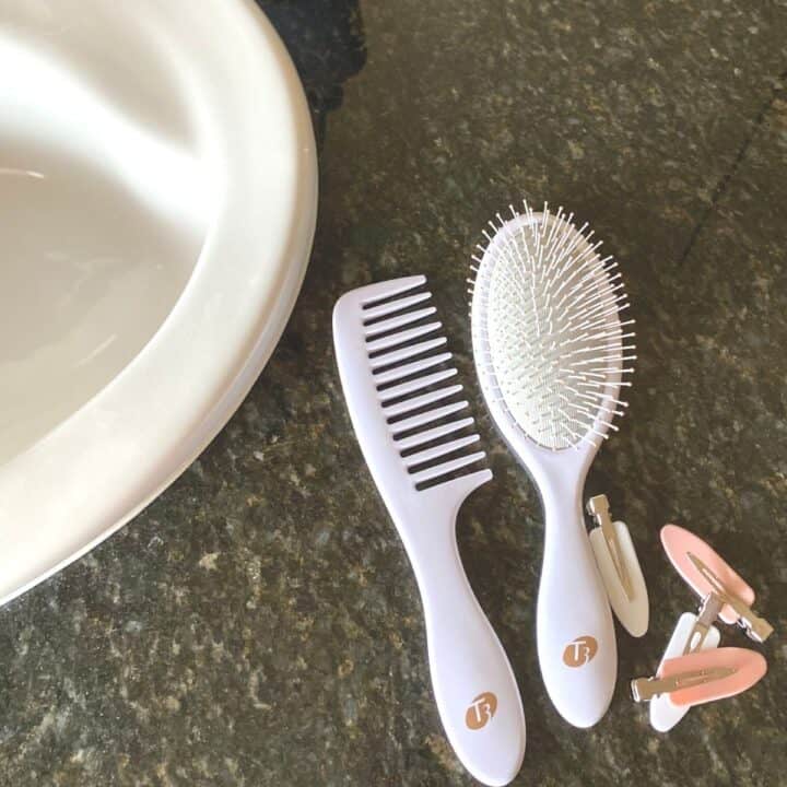 Bathroom countertop with styling tools laid out, including a white wide-tooth comb, white hairbrush and a mix of white and rose pink barrettes