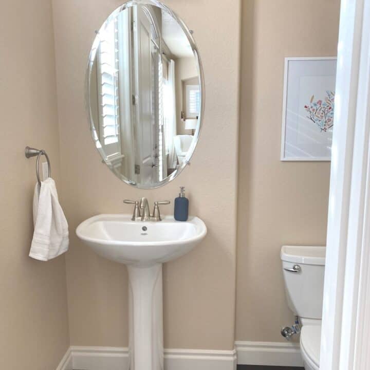 Powder bath with an oval mirror above a pedestal sink. This image is meant to depict using rubbing alcohol to clean mirrors and glass.