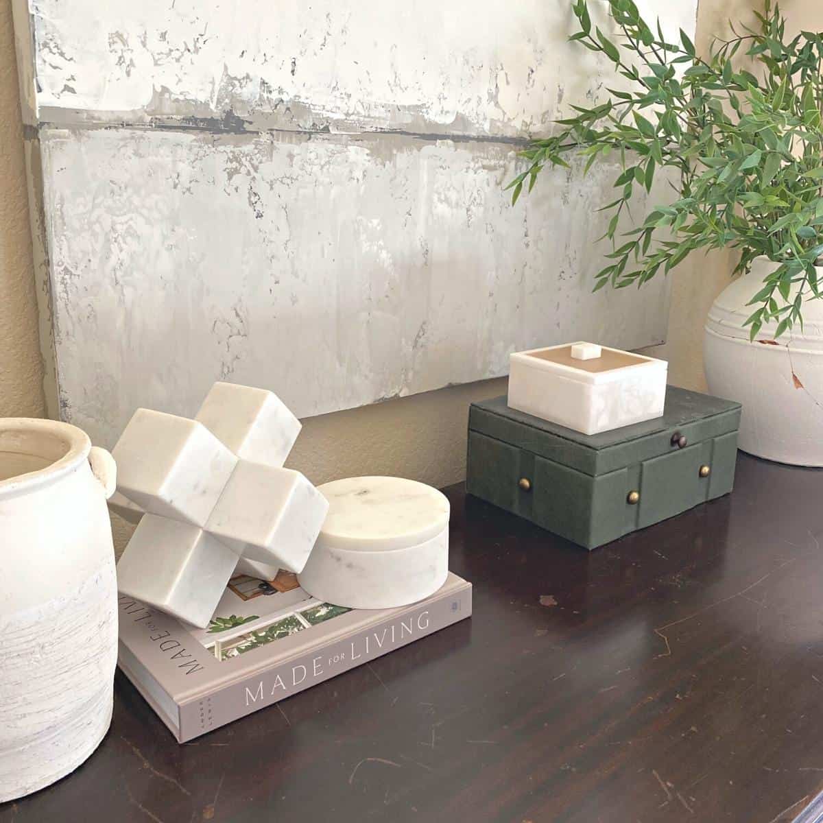 Console table styled with a white vase, marble objects on top of a book and next to two stacked boxes.