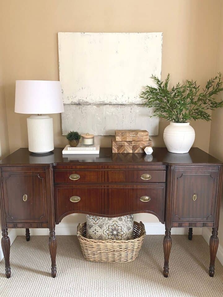 Vintage solid wood buffet table, styled as a console table. The table includes a lamp, decor, books, stacked wood boxes, a large white vase, and artwork. 