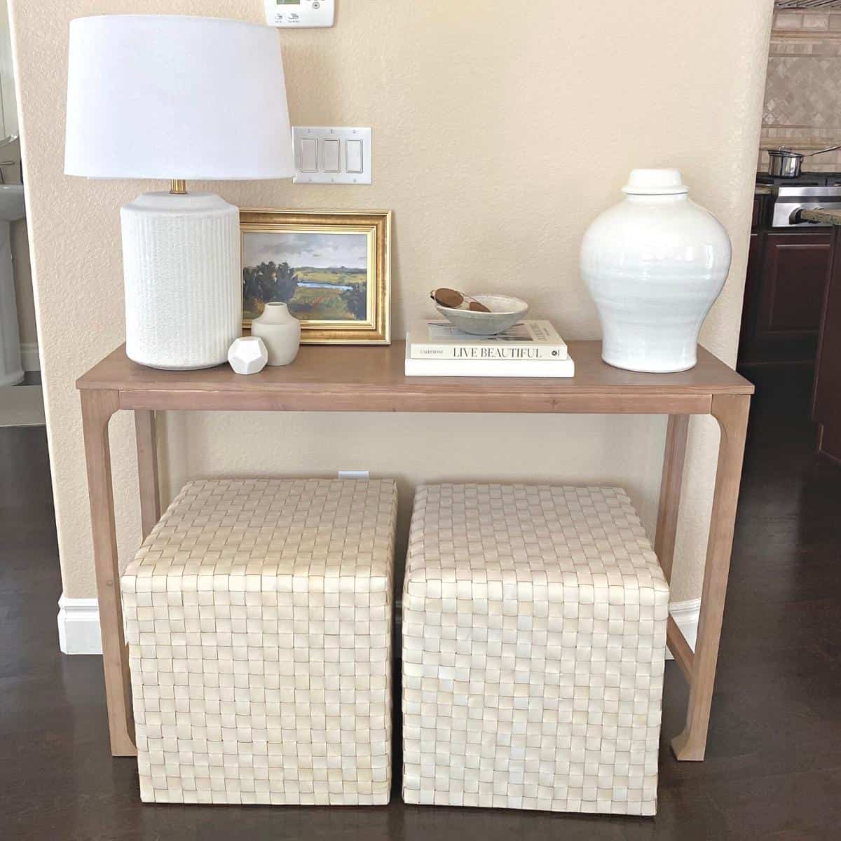 Console table styled with a white textured lamp on the left, small framed art next to pretty coffee table books with a grey textured bowl set on top and a large white vase on the right