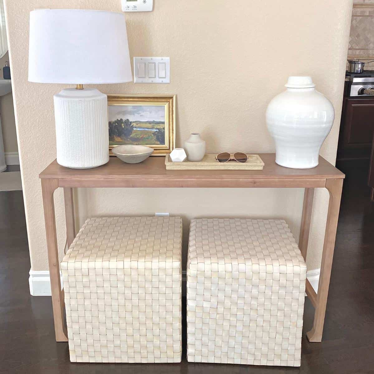 Console table styled with a white textured lamp on the left, small framed art and a tray of home decor accessories in the middle and a large white vase on the right