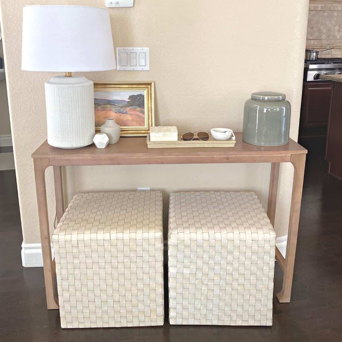 Console table styled with a white textured lamp on the left, small framed art and a tray of home decor accessories in the middle and a medium size sage green vase on the right