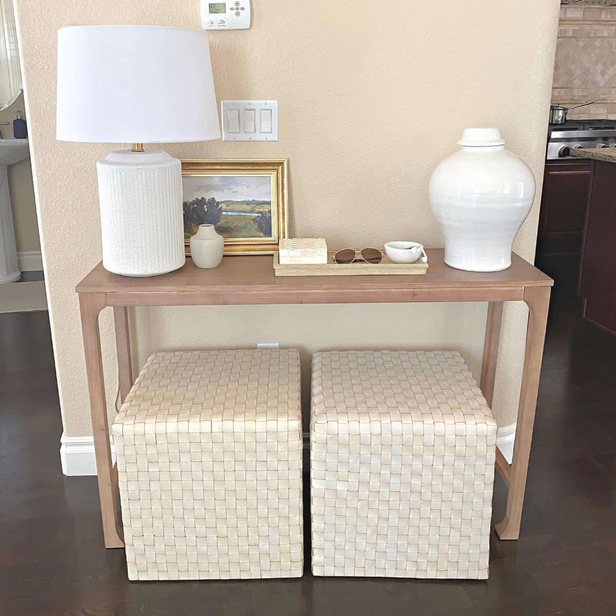 Console table styled with a white textured lamp on the left, small framed art and a tray of home decor accessories in the middle and a large white vase on the right