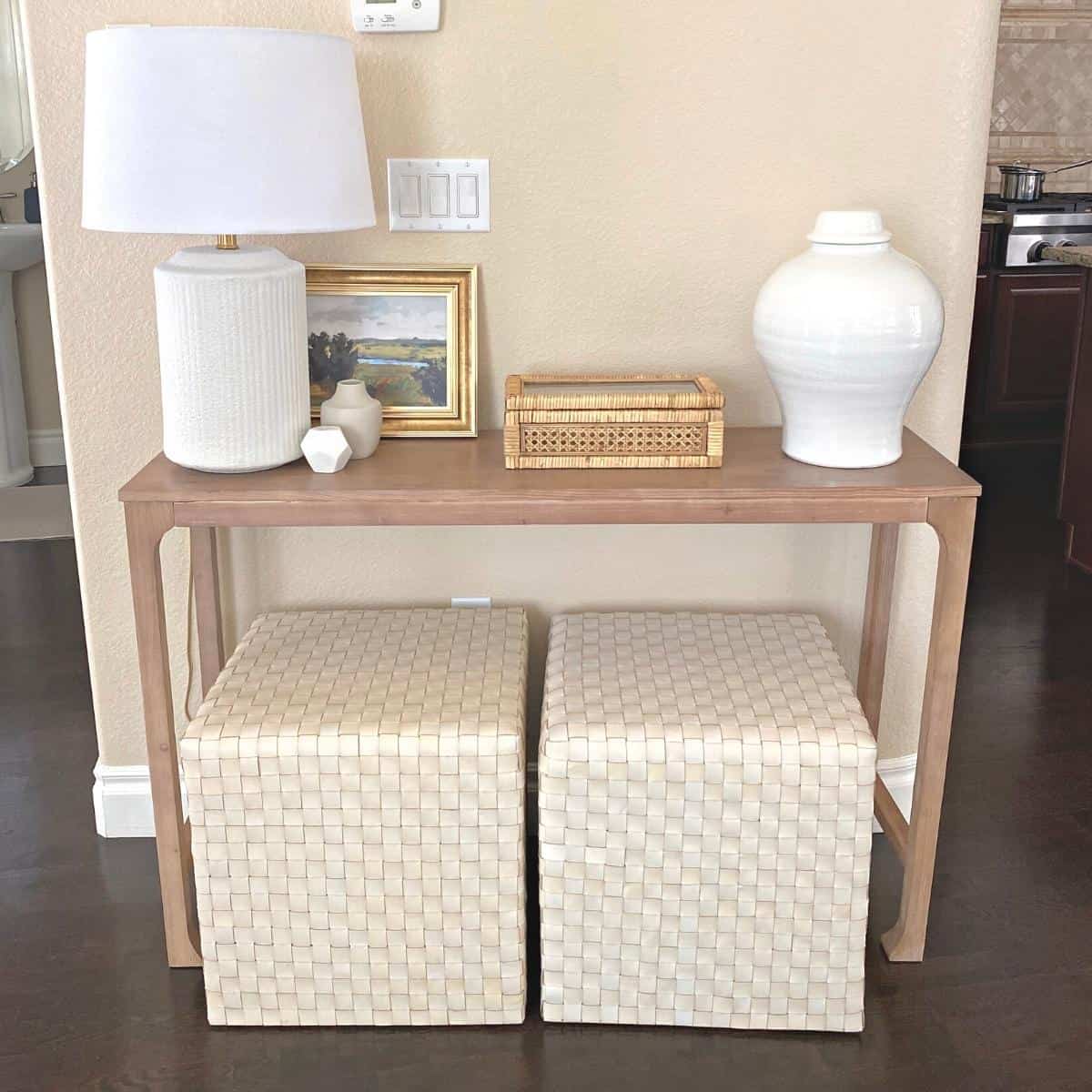 Console table styled with a white textured lamp on the left, small framed art next to a rattan box in the middle and a large white vase on the right