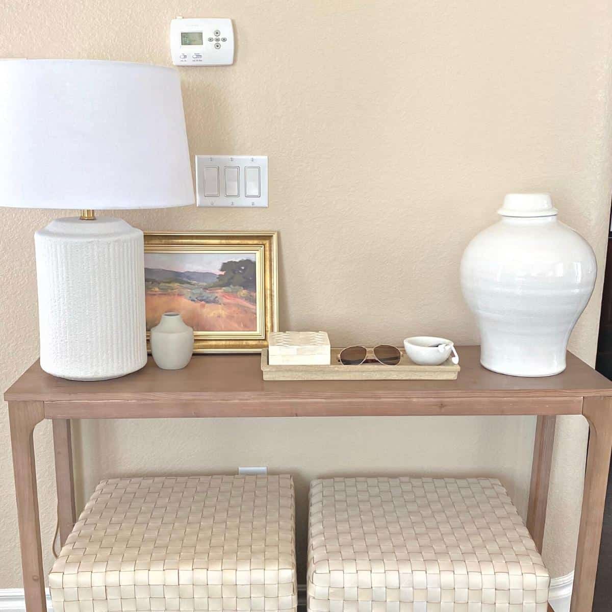 Console table styled with a white textured lamp on the left, small framed art and a tray of home decor accessories in the middle and a large white vase on the right