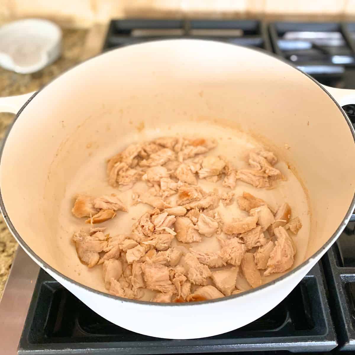 cut up cooked chicken in white cast iron pot