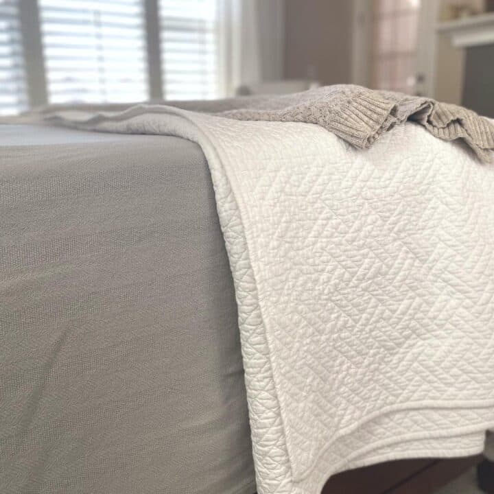 Close up of a white diamond pattern organic cotton coverlet over a grey herringbone organic cotton bed blanket