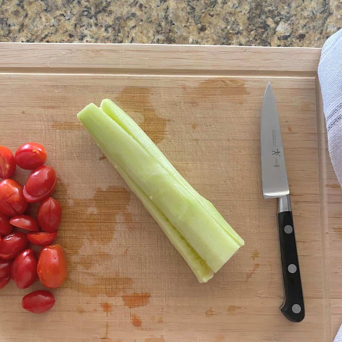 Sliced cucumber and diced tomatoes for salad on a cutting board next to a knife