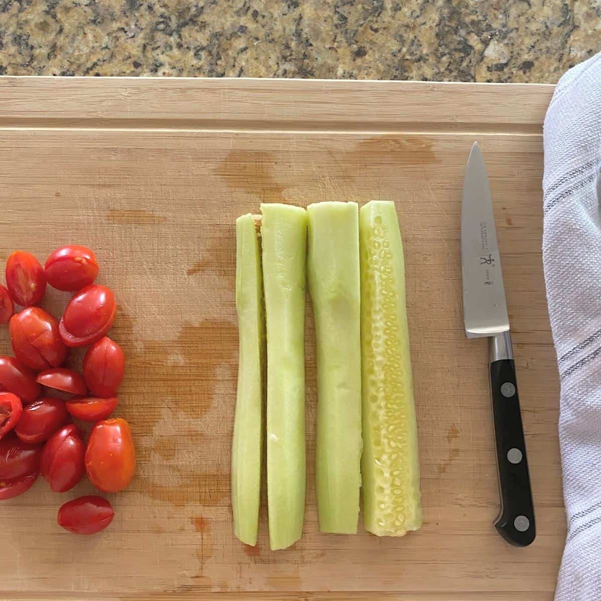 Quartered cucumber and tomatoes for salad on a cutting board next to a knife