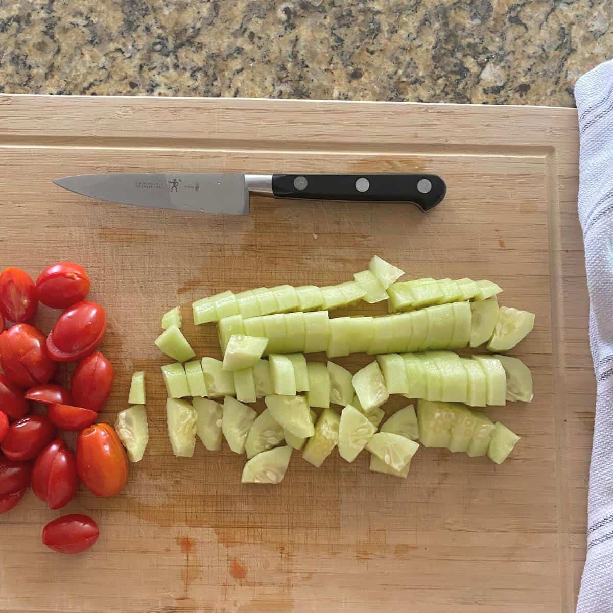 Diced and quartered cucumber and tomatoes for salad on a cutting board next to a knife