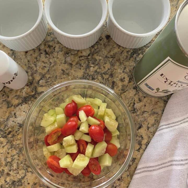 Cucumber and tomato salad in a glass mixing bowl, with white ramekins, olive oil and salt
