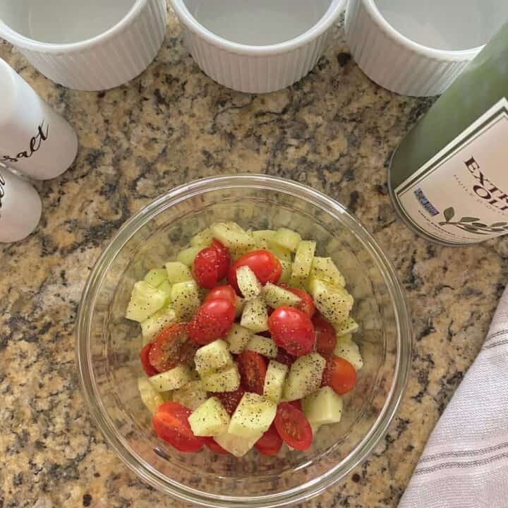 Cucumber and tomato salad in a glass mixing bowl, with white ramekins, olive oil and salt & pepper