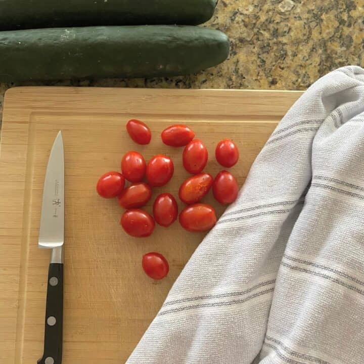 Tomatoes on top of a bamboo cutting board with a pairing knife and Turkish towel nearby