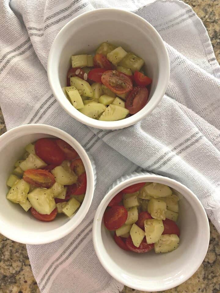 Cucumber tomato salad served in three white ramekins, flanked atop by white salt and pepper shakers and a tin container of olive oil.