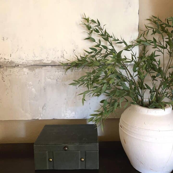 Background is canvas artwork by Sarah Brooke in the Adrift series. A green felt, velvet box with brass buttons sits in front, with a large white terracotta vase off to the right.