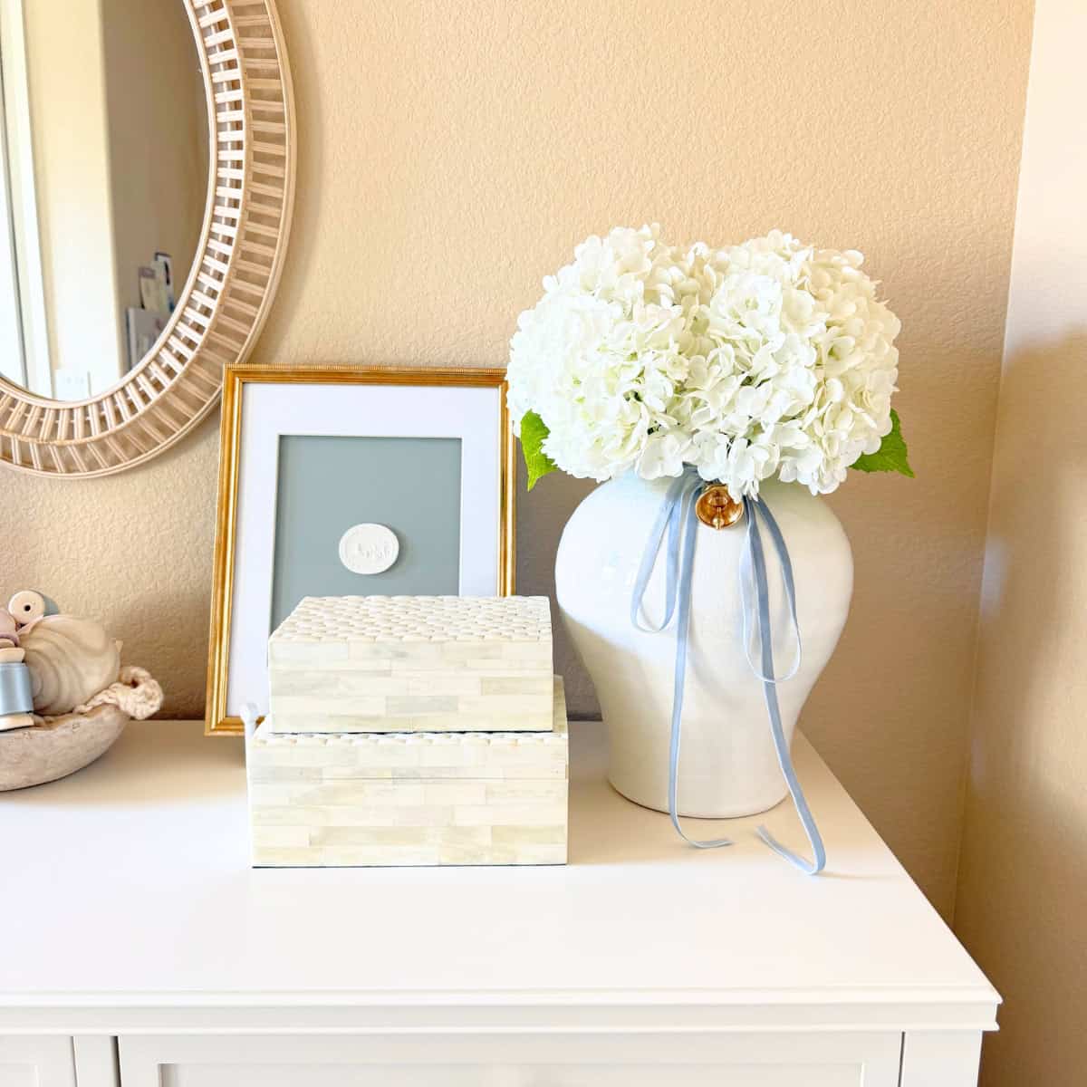 large white vase with faux flowers and other decor atop a dresser