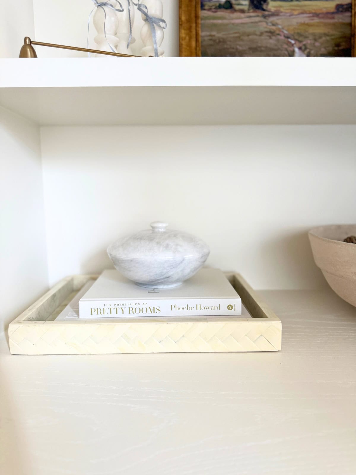 round marble dish with lid atop books in a tray on bookshelves
