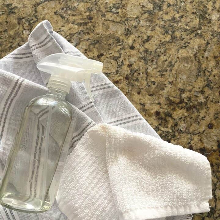 Spray bottle next to kitchen towels, with diluted rubbing alcohol used to sanitize kitchen countertops