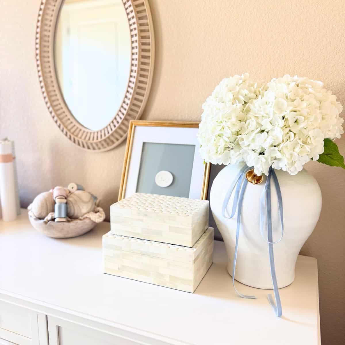 large white vase with faux flowers and other decor atop a dresser