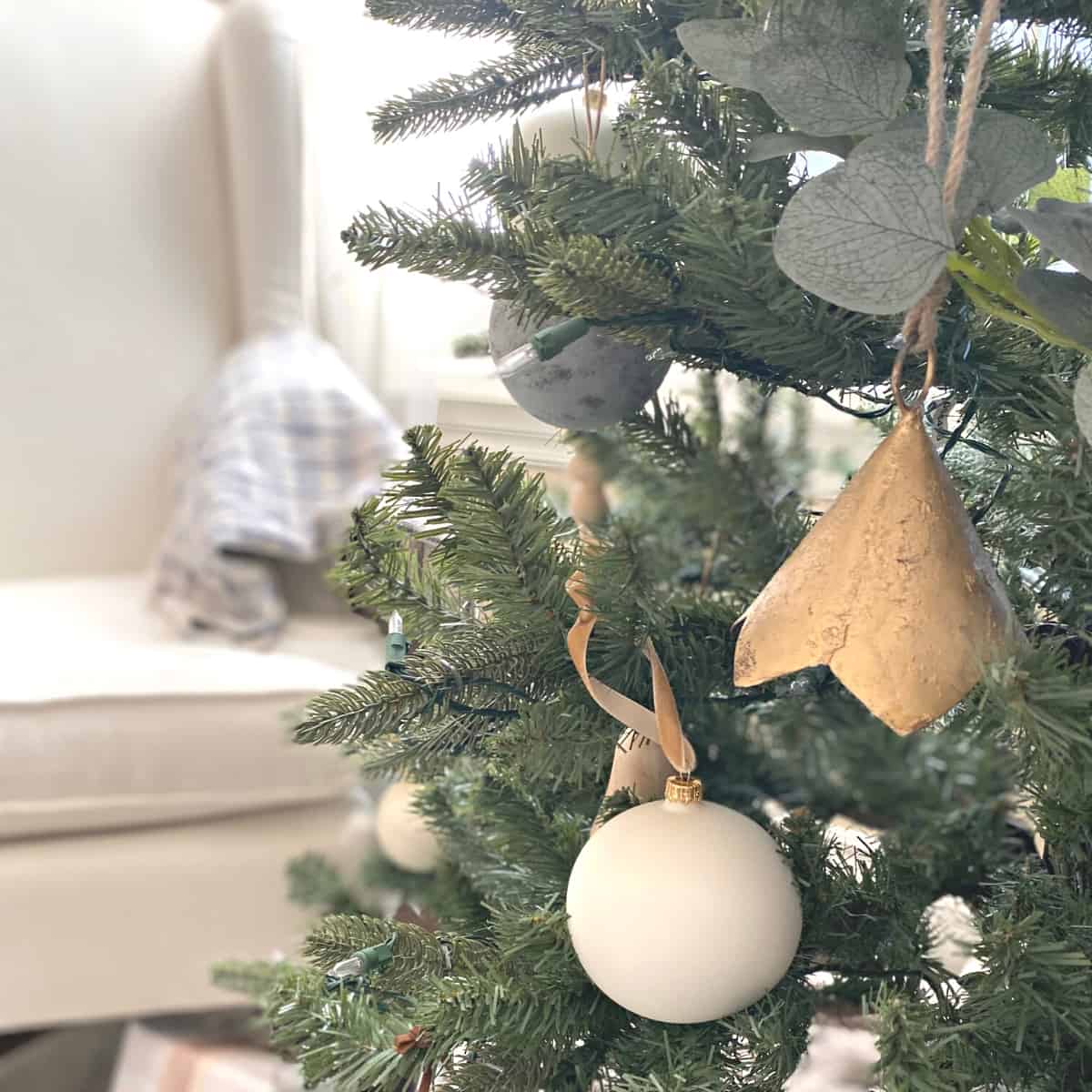 Eucalyptus garland weaved into a Christmas tree with neutral ornaments of brass bells and a white glass ball