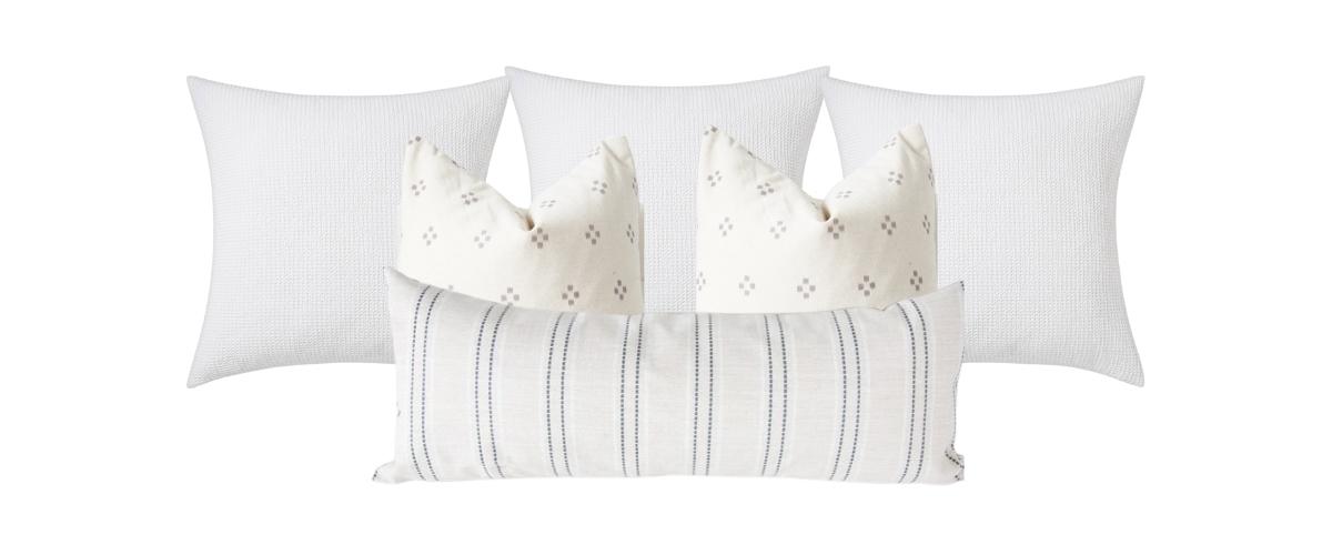 Set of throw pillows for a king size bed. Three all white euro pillows in the back, two twenty-four inch square gray dot block print patterned pillows in the middle and an oversized lumbar pillow in a gray-beige stripe in the front.