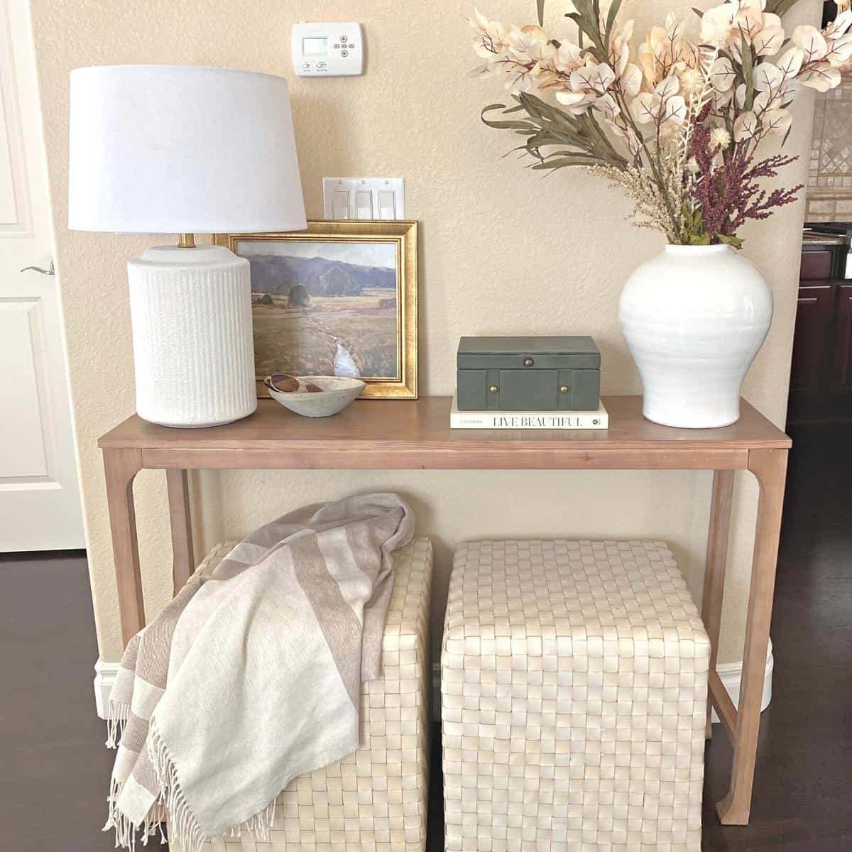 Console table decorated for fall with floral stems, a gold framed green artwork, white lamp and dark green felt covered box with brass hardware on top of a neutral book