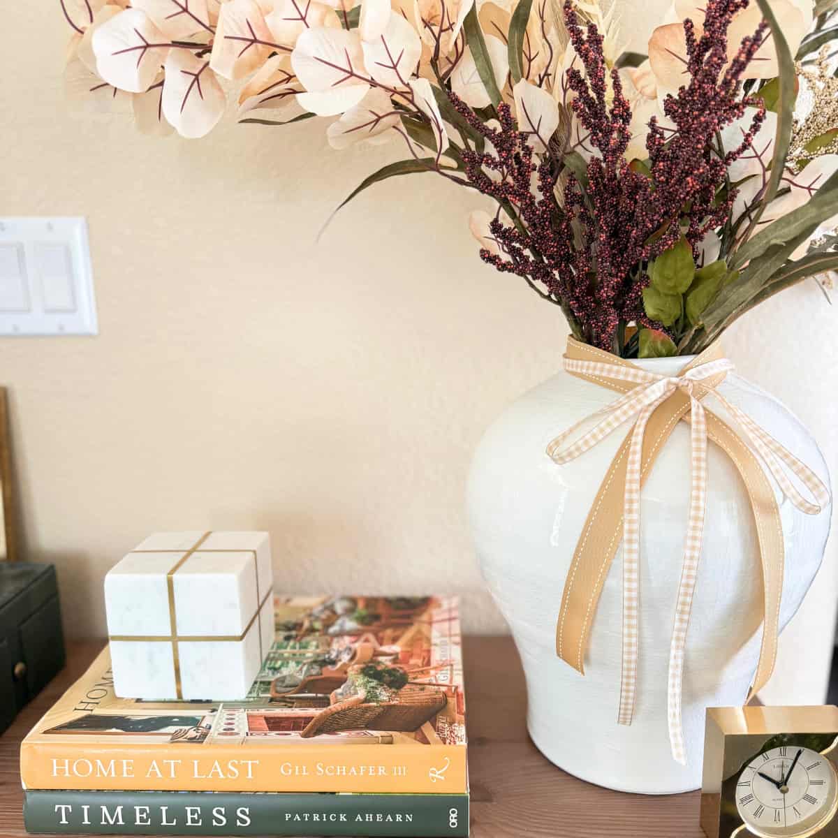 console table styled for fall with ochre book and white vase with various fall colored stems