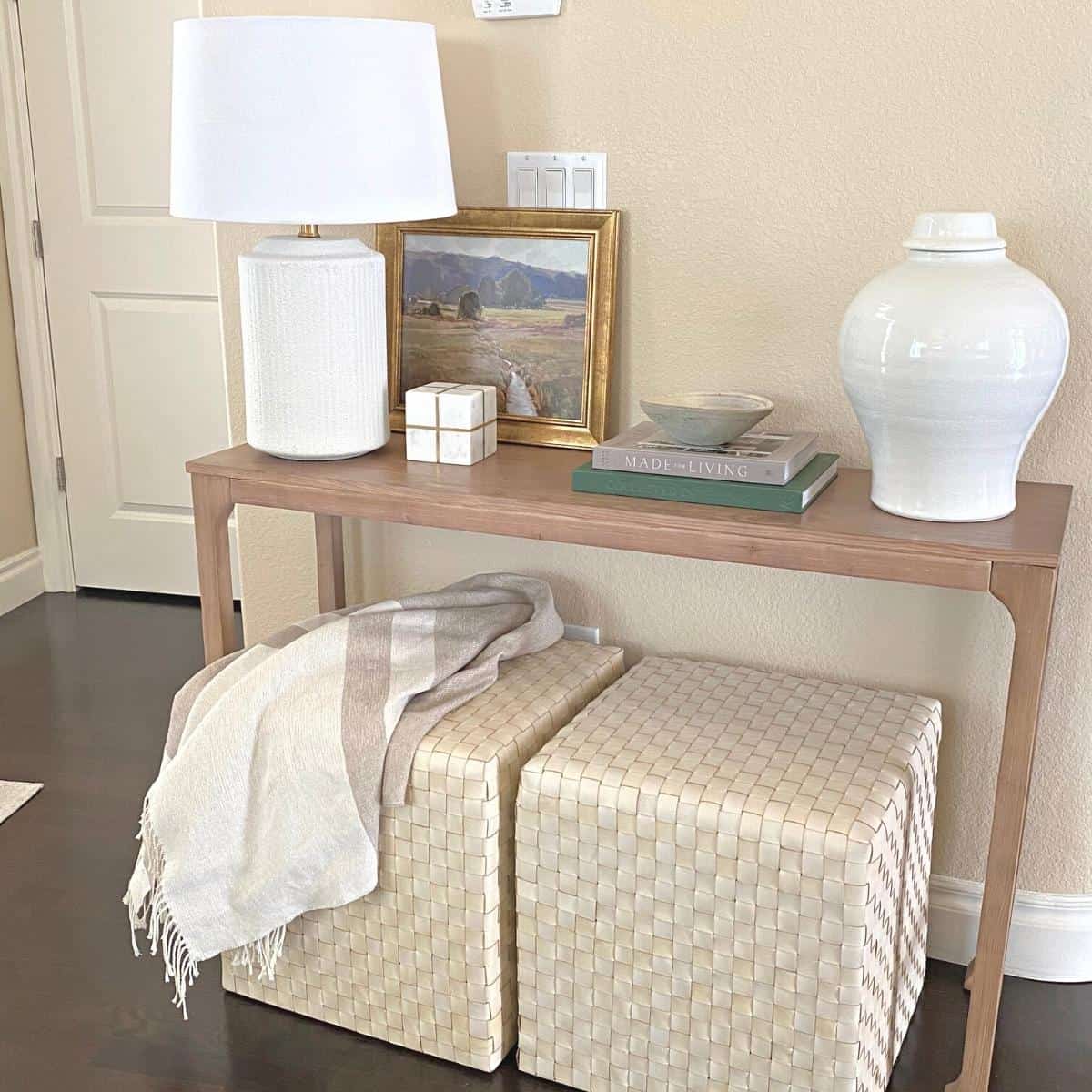 Console table decorated for fall with floral stems, a gold framed green artwork, white lamp and marble brass object. Two books on top next to a white vase.